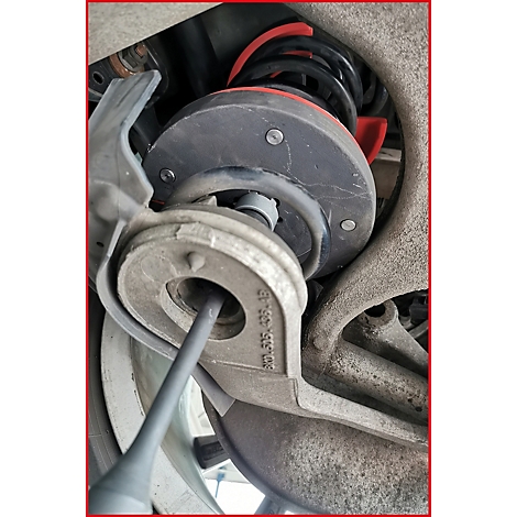 Nahaufnahme eines Fahrwerksteils. Eine Feder, eine Stoßdämpferhalterung und andere Metallteile sind zu sehen.